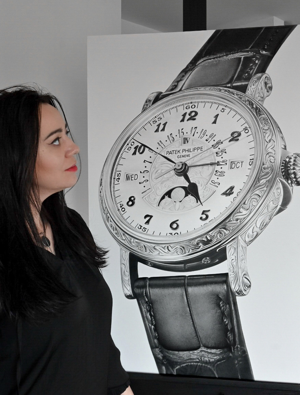 Sinziana Iordache standing and observing one of her hyperrealistic luxury watch art drawings in graphite, the Patek Philippe 5160 Grand Complications Perpetual Calendar, displayed on an easel.